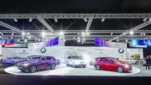 Auf einer hell erleuchteten Autoshow stehen mehrere BMW Hybridfahrzeuge in verschiedenen Farben, mit Informationsschildern, Oberlichtern und einigen Zuschauern im Hintergrund.