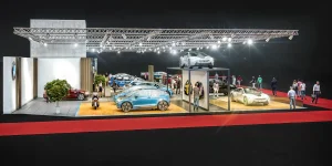 Auf einer hell erleuchteten Vienna Auto Show stehen BMW Elektrofahrzeuge und ein E-Roller auf erhöhten Plattformen, auf denen die Menschen spazieren gehen und die Fahrzeuge beobachten; ein roter Teppich säumt die Ausstellungsfläche.