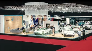 Ein weißes BMW i8 wird auf einer Plattform aus Glas auf der Vienna Autoshow 2019 ausgestellt. Mehrere Personen in Geschäftskleidung stehen um das Auto herum, und moderne Beleuchtung und Großprints schmücken den Hintergrund.