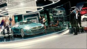 Ein tealfarbenes BMW 8er wird auf einer kreisrunden Plattform bei der Vienna Autoshow 2019 ausgestellt. Mehrere Personen in Geschäftskleidung stehen um das Auto herum, und moderne Beleuchtung und Großprints schmücken den Hintergrund.