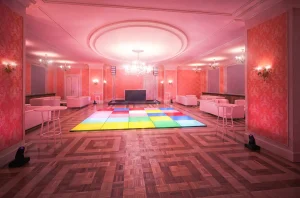 Disco Bereich einer Hochzeitsverantaltung mit Stucko und Textiltapeten mit intensivem Rosa Licht und bunter LED Tanzfläche. Links und rechts sind Sofas und Sesseln aufgestellt