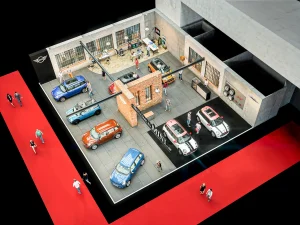 Ansicht aus der Vogelperspektive der MINI Ausstellungsfläche auf der Vienna Autoshow 2017. Mehrere Menschen beobachten die ausgestellten Fahrzeuge. Im Zentrum des Messestandes ist eine rote Ziegelwand. Ein roter Bodenbelag umgibt Ausstellungsfläche.