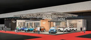 Ansicht der MINI Ausstellungsfläche auf der Vienna Autoshow 2017. Mehrere Menschen beobachten die ausgestellten Fahrzeuge. Im Zentrum des Messestandes ist eine rote Ziegelwand. Ein roter Bodenbelag umgibt Ausstellungsfläche.