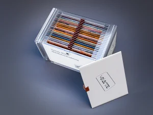 Blechmuster Box aus Acrylglas mit einem magnetischen Verschluss aus Leder, Box ist offen. In der Box sind mehrere Blechmuster und ein Folder. Blick ist von oben in die Box.