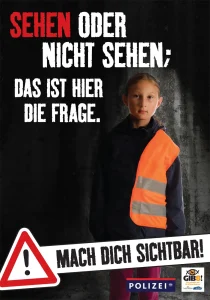 Plakat mit einem Mädchen auf dunklem Hintergrund, sie hat eine Jacke halb sehr dunkel und halb Sicherheitsveste mit reflektierenden Streifen.