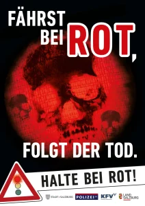 Ein Plakat mit dem Bild des roten Lichtes einer Ampel und einem stilisierten Totenkopf darüber. Text am Plakat ist: Fährst bei Rot, folgt der Tod. Halte bei Rot!