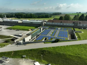 Photovoltaik Anlage auf einem flachen Gebäude, Besucherzentrum in der Gedenkstätte Mauthausen, umgeben von Grasflächen, Vogelperspektive mit der Gedenkstätte Mauthausen im Hintergrund