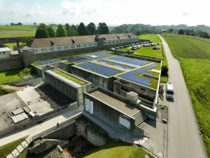 Photovoltaik Anlage auf einem flachen Gebäude, Besucherzentrum in der Gedenkstätte Mauthausen, umgeben von Grasflächen, Vogelperspektive mit Bäumen im Hinergrund