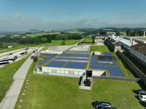 Photovoltaik Anlage auf einem flachen Gebäude, Besucherzentrum in der Gedenkstätte Mauthausen, umgeben von Grasflächen, Vogelperspektive mit Hügellandschaft im Hinergrund