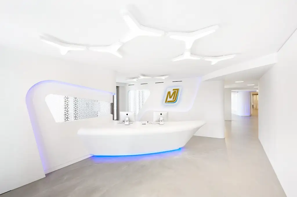 Interieur eines futuristisch gestalteten Empfangsbereich einer Zahnärztlichen Tagesklinki mit weißen Wäden und Dekorationselementen, Empfangspult mit einem blauen Neonschein an der Bodenkante